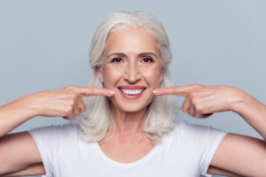 Close up of happy older female pointing to clean white teeth